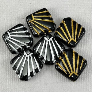 May include: Six black square glass beads with a geometric design. The beads have a gold or silver metallic finish.