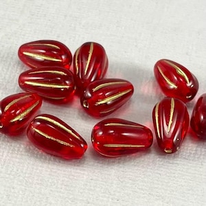 Könnte beinhalten: Eine Ansammlung roter, tropfenförmiger Perlen mit goldfarbenen Streifen. Die durchscheinenden Perlen eignen sich für die Schmuckherstellung und Bastelprojekte. Jede Perle ist etwa 1,5 cm lang.
