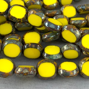 May include: Close-up of a collection of yellow and brown beads. Each bead has a bright yellow center and a mottled, metallic brown and gray outer ring. The beads are irregularly shaped, suggesting a natural or handcrafted aesthetic.