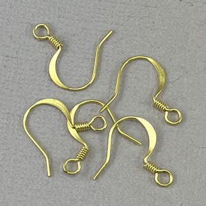 May include: Close-up of several gold-colored earring hooks. Each hook has a curved design with a looped end and a coiled wire detail. The hooks are arranged on a light gray surface.