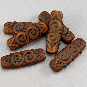 May include: Six brown ceramic beads with a swirl design. The beads are approximately 2.5 cm long and have a textured surface.