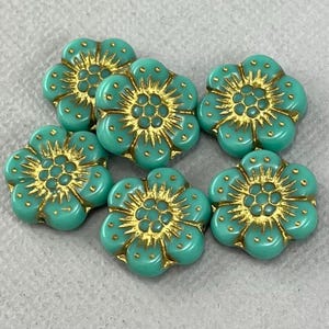 May include: Six turquoise glass flower beads with gold accents. The beads are approximately 1 inch in diameter and have a raised flower design.