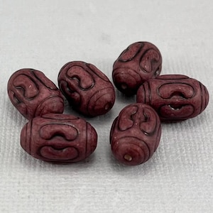May include: Six dark red oval-shaped beads with a carved design. The beads are made of a smooth, polished material.