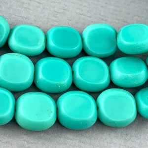 May include: A strand of turquoise blue oval-shaped glass beads. The beads are smooth and have a slightly rounded edge.