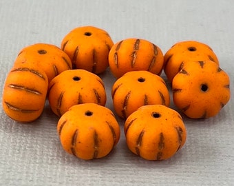 Puede incluir: Diez cuentas de color naranja en forma de calabaza con una superficie texturizada y un pequeño agujero para enhebrar. Las cuentas tienen un glaseado marrón.