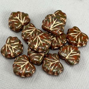 May include: A collection of 12 brown and green glass leaf-shaped beads with gold accents. The beads are perfect for jewelry making or crafting.