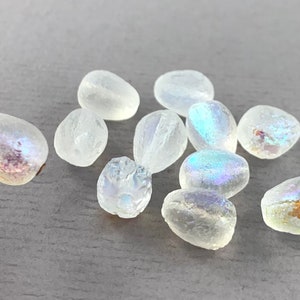 May include: A collection of iridescent white glass beads, some with a pearlescent finish. The beads are oval shaped and have a smooth, polished surface.