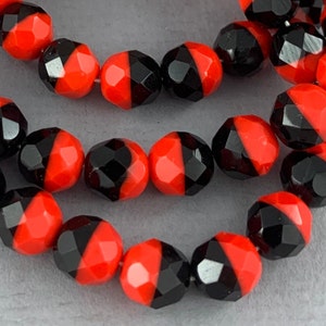 May include: Close-up of a strand of faceted beads. Each bead is divided into two halves, one bright red and the other black. The beads are strung together, creating a visually striking pattern. The beads are likely for jewelry making.