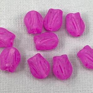 May include: Eight small, translucent, bright pink beads shaped like tulip flower buds. Each bead features a molded, textured surface with vertical ridges that mimic the appearance of flower petals, with a small hole visible at the base of each.