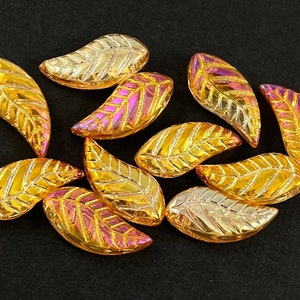 May include: A collection of ten iridescent glass leaf-shaped beads in shades of gold and pink. The beads have a textured surface and are perfect for jewelry making or crafting.