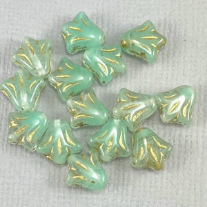 May include: A collection of seafoam green star-shaped beads with gold accents. The beads have a pearlescent finish and a unique, fan-like gold design. These beads are ideal for jewelry making and crafting projects.