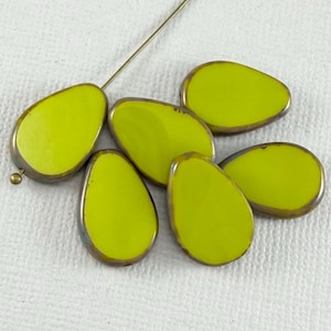 May include: Six lime green teardrop-shaped beads with a metallic bronze-colored edge. A gold-colored head pin is inserted through one bead. The beads are smooth and glossy, ideal for jewelry making or crafting projects.