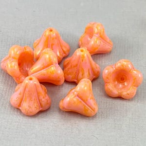 May include: A collection of orange flower-shaped beads with a glossy finish. The beads have a hole for stringing and are suitable for jewelry making or craft projects. The beads have a textured surface and a gradient of orange and pink.