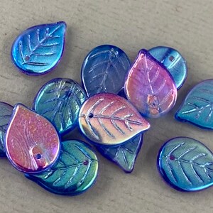 May include: A collection of iridescent leaf-shaped beads in shades of blue, green, and purple. Each bead has a detailed leaf vein pattern and a small hole for stringing. These decorative beads are ideal for jewelry making and craft projects.