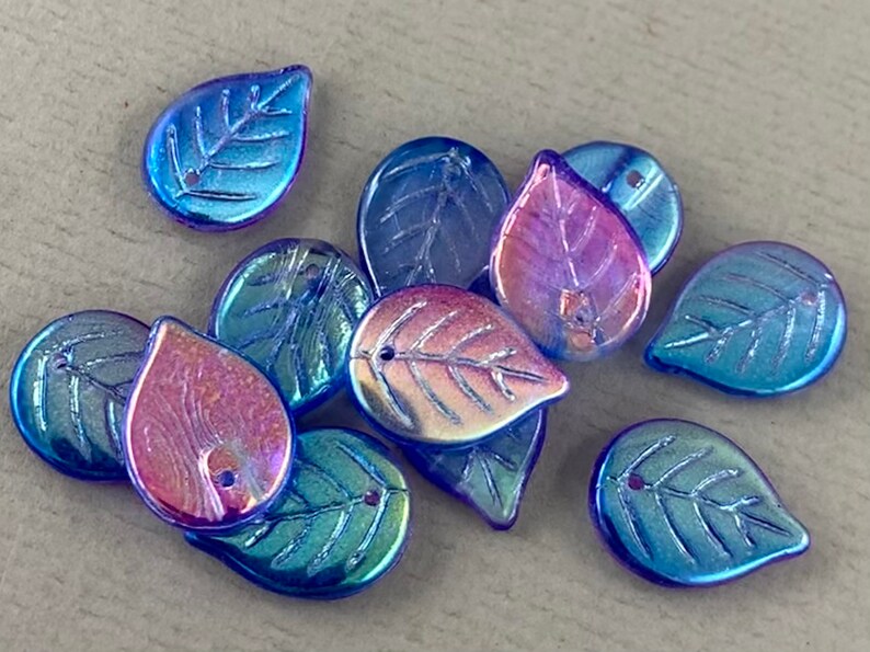 May include: A collection of iridescent leaf-shaped beads in shades of blue, green, and purple. Each bead has a detailed leaf vein pattern and a small hole for stringing. These decorative beads are ideal for jewelry making and craft projects.