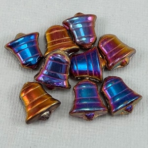 May include: A collection of iridescent bell-shaped beads. The beads have a metallic finish with colors shifting from blue to purple and gold. Each bead has a small loop at the top and a rounded base. The beads are scattered on a light-colored surface.