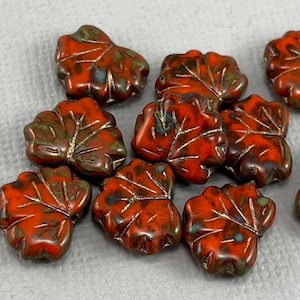 May include: A collection of leaf-shaped beads in shades of red, brown, and green. The beads have a glossy finish and detailed vein patterns. These decorative beads are ideal for jewelry making and other craft projects.