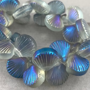 May include: A strand of iridescent glass beads shaped like seashells. The beads are a mix of clear and blue iridescent colors.