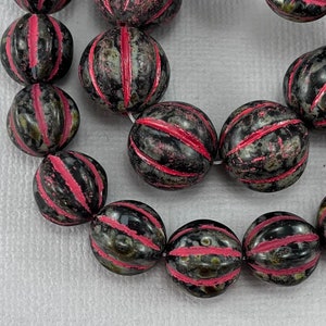 May include: A strand of black and pink striped round beads. The beads have a mottled, speckled appearance.