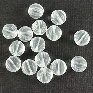 May include: A collection of clear glass beads with a ribbed texture. The beads are round and have a translucent appearance.