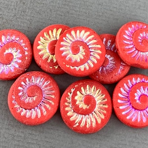 May include: A group of eight red glass beads with a gold and iridescent pink spiral design. The beads are round and flat, and they have a smooth, glossy finish.