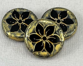 May include: Three round, decorative beads with a black flower design. The beads have a gold and black color scheme with a distressed, crackled finish. The flower has five petals and a central dot.