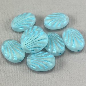 May include: A group of eight oval-shaped glass beads with a light blue iridescent finish. The beads have a raised, fan-shaped design.
