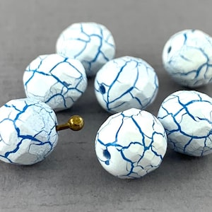 May include: A group of seven white glass beads with blue crackle glaze. The beads are faceted and have a slightly irregular shape.