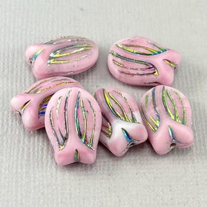 Op de afbeelding: Zes roze glazen kralen met iriserende accenten. De kralen zijn gevormd als tulpblaadjes, met gebogen lijnen en een glanzende afwerking. De kralen zijn lichtroze van kleur met strepen van goud, groen en blauw.