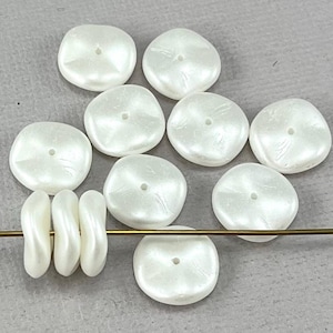 May include: Ten white, round, flat, iridescent, plastic beads with a hole in the centre. The beads are arranged in a semi-circle with three beads stacked on top of each other.