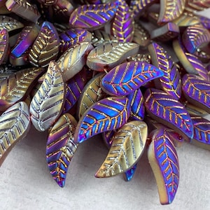 May include: A pile of iridescent glass leaf-shaped beads in shades of gold, purple, and blue. The beads have a textured surface with a leaf pattern.