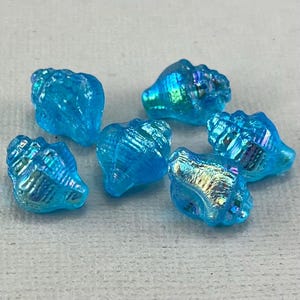 May include: Six iridescent blue glass seashells. The shells are shaped like a conch and have a shiny, iridescent finish.