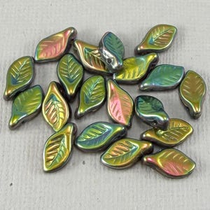 May include: A collection of iridescent leaf-shaped beads. The beads have a metallic sheen with colors ranging from green and gold to pink and blue. Each bead features a detailed leaf vein pattern.
