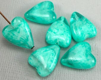 May include: Seven heart-shaped beads in shades of turquoise and white. The beads have a marbled appearance and a glossy finish. One bead has a brown stem attached. These beads are suitable for jewelry making.