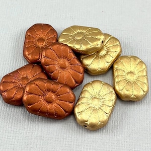 May include: A collection of metallic beads in shades of copper and gold. Each bead has a rectangular shape with a floral design on the surface. These beads are suitable for jewelry making and craft projects.