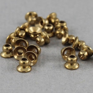 May include: A group of gold-colored metal beads with a small hole in the center of each bead. The beads have a rounded top and a flat bottom.