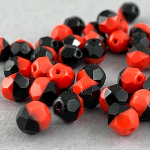 May include: A collection of red and black faceted glass beads. The beads are half red and half black, with a sharp contrast between the two colors.