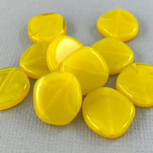 May include: A group of ten yellow glass beads with a swirl pattern. The beads are oval shaped and have a glossy finish.