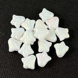 May include: A group of white iridescent glass beads in the shape of a flower. The beads have a slightly textured surface and are arranged in a pile.