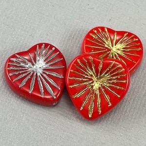 May include: Three red heart-shaped glass beads with gold and silver starburst designs.