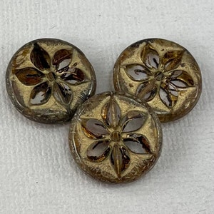 May include: Three round, brown glass buttons with a gold-colored flower design. The buttons have a raised, textured design and are translucent.