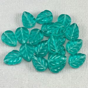 May include: A collection of teal glass leaf beads. The beads are translucent and have a slightly frosted finish.