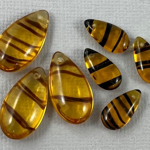 May include: Eight amber glass teardrop-shaped beads with black stripes. The beads have a hole at the top for stringing.