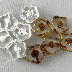 May include: A collection of ten clear glass flower-shaped buttons. Five buttons are clear with iridescent accents, and five buttons are clear with gold accents.