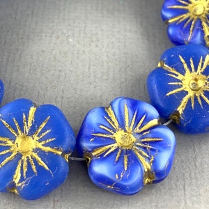 Könnte beinhalten: Eine Reihe von blauen Glasblumenperlen mit goldenen Akzenten. Die Perlen sind auf einem durchsichtigen Faden aufgefädelt.