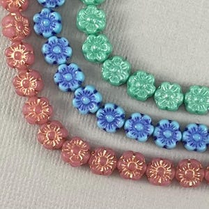 May include: Three strands of flower-shaped beads in pink, blue, and green. The beads are all the same size and shape, and they are strung together on a clear string.