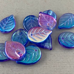 May include: A collection of iridescent leaf-shaped beads. The beads have a blue and purple color shift, with visible leaf vein details. Each bead has a small hole for stringing. These beads are suitable for jewelry making and craft projects.
