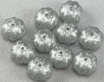 May include: A group of ten silver-colored, flower-shaped beads with a textured surface.
