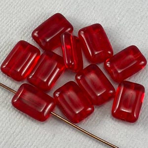 Könnte beinhalten: Zehn rote Glasperlen in rechteckiger Form. Die Perlen sind durchscheinend und haben einen leichten Schimmer.