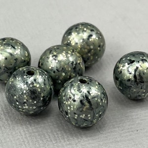 May include: Six round, grey beads with a speckled, glittery finish. The beads are approximately 2.5 cm in diameter.
